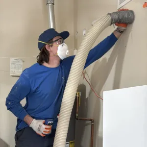 HVAC technician using drill-and-fill method to inject insulation into existing garage wall cavities in Gilbert, Arizona