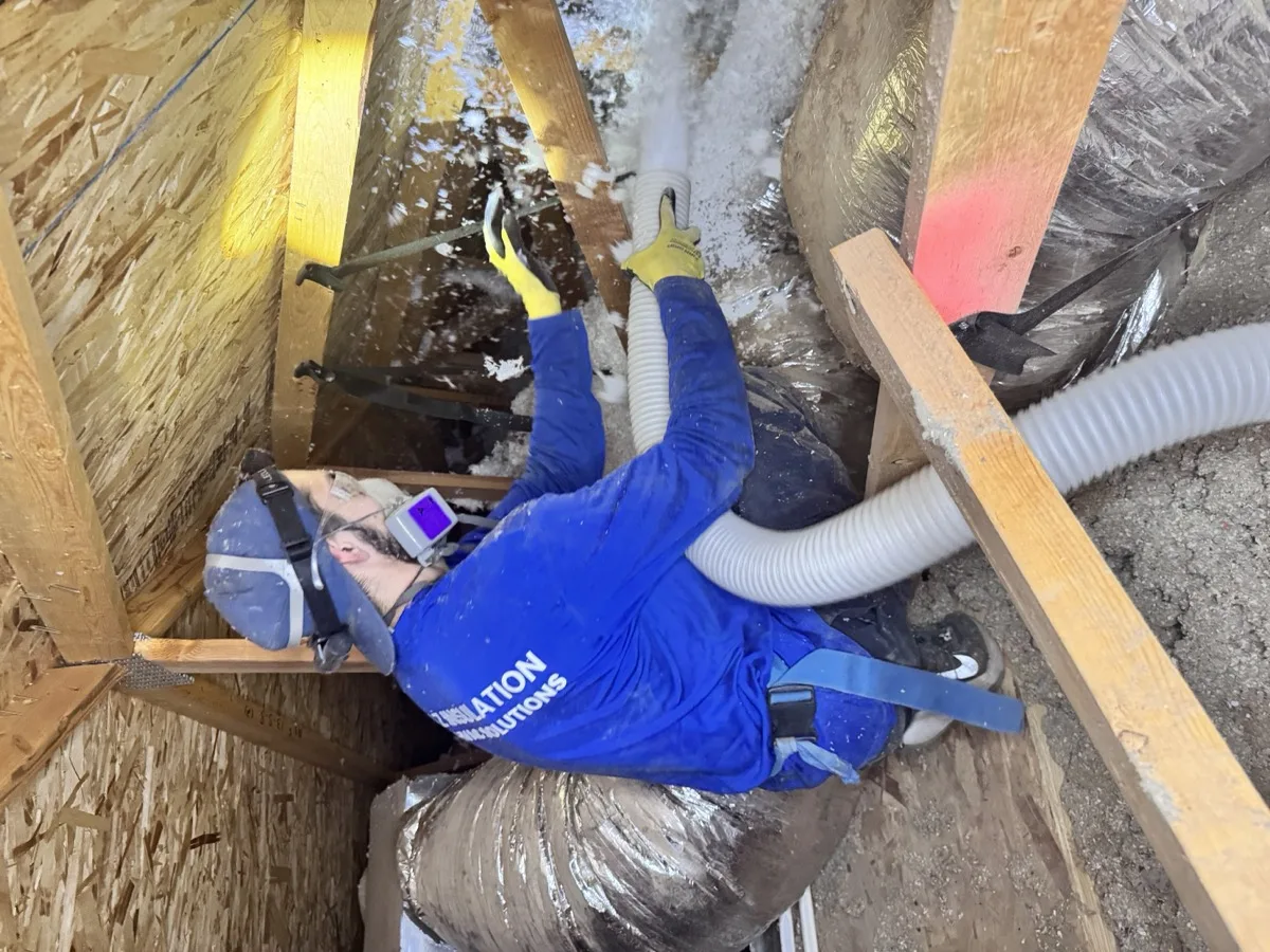 An AZ Insulation technician in a respirator blowing loose-fill fiberglass to R-38 around the ductwork in an Arizona attic.