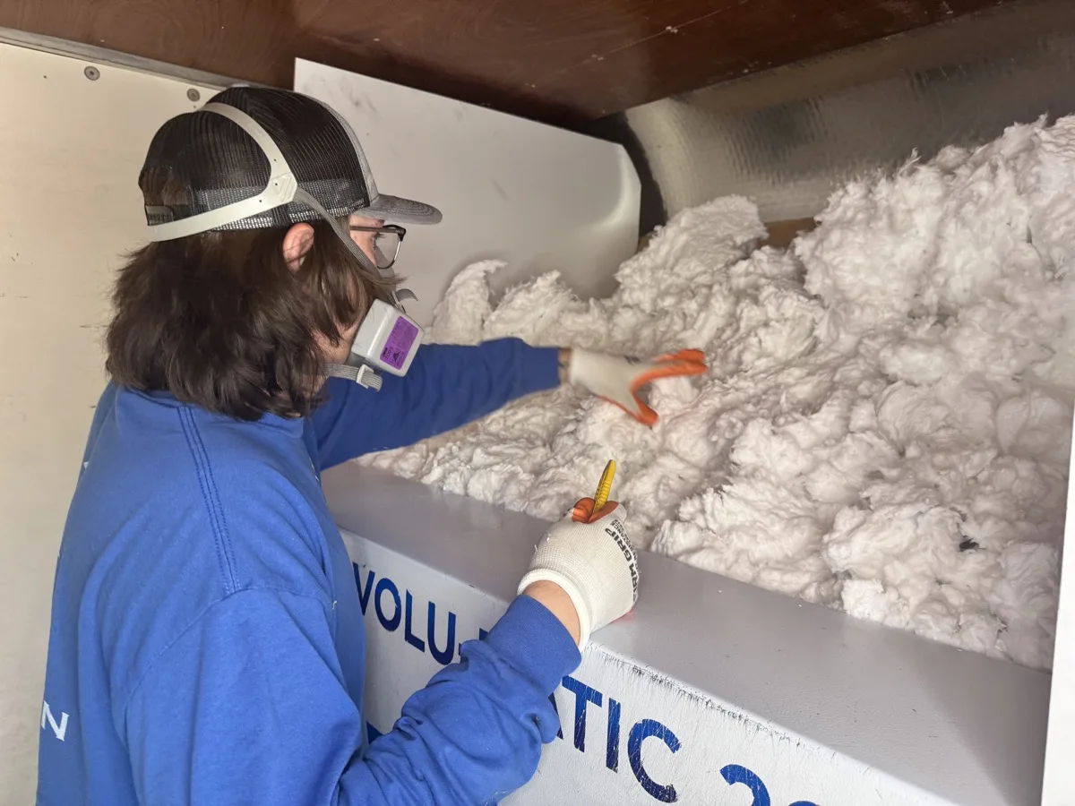 An AZ Insulation technician loading loose-fill fiberglass into the hopper of a blowing machine on the job site.