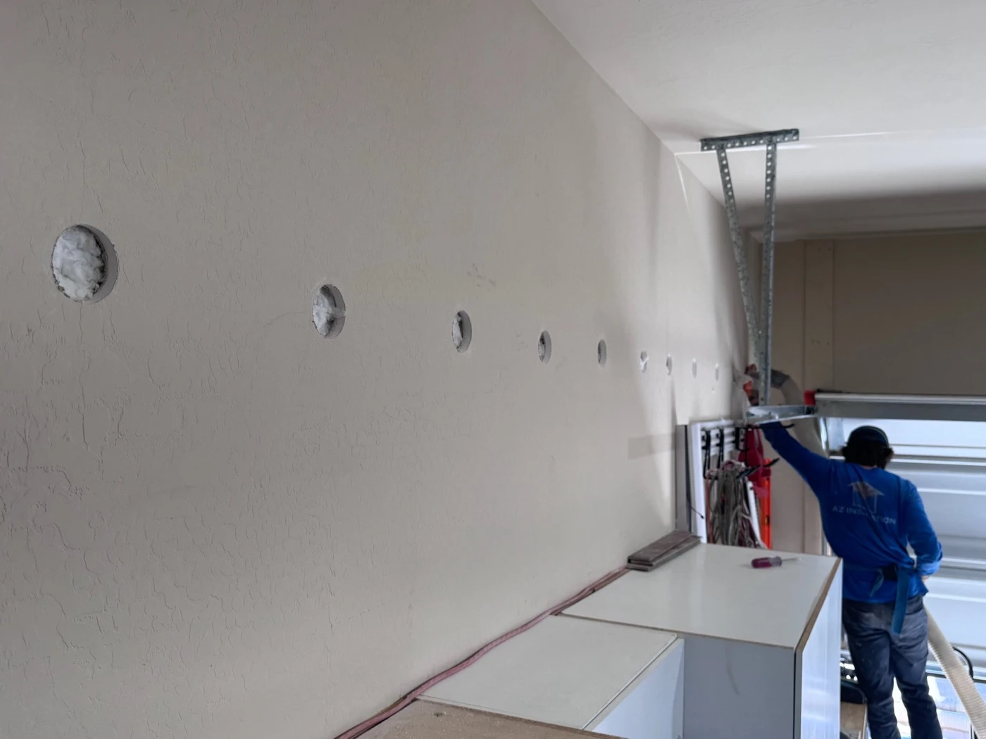 A row of small drilled holes along a garage wall in a Phoenix, AZ home, dense-packed with insulation before patching.
