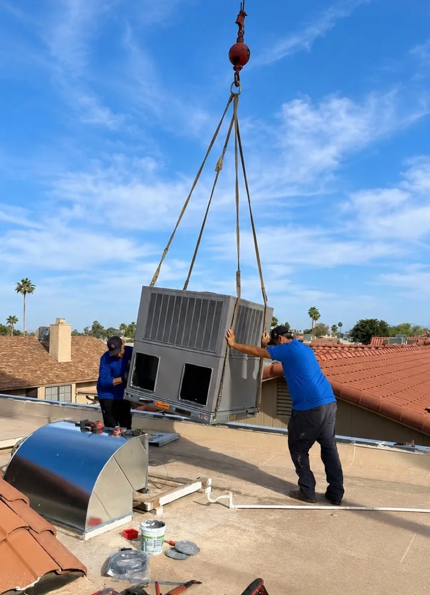 Two AZ Insulation technicians guiding a new high-efficiency packaged HVAC unit into place by crane on an Arizona rooftop.